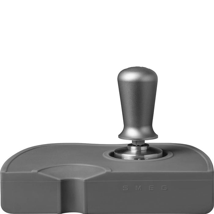 Grey, stainless steel Smeg tamper and portafilter holder with a stainless steel Smeg tamper in tamper spot on a white background