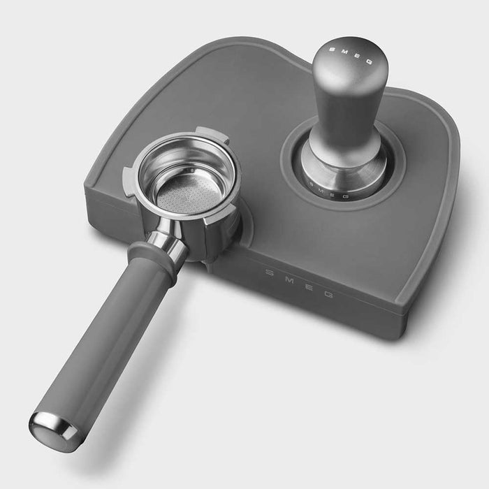 Grey, stainless steel Smeg tamper and portafilter on a white background