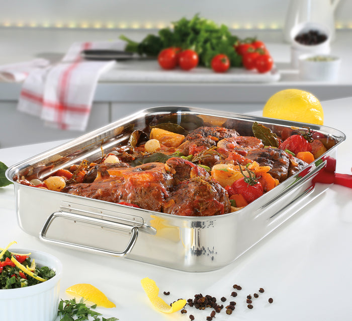 Stainless steel roasting pan with roasted vegetables on a kitchen counter