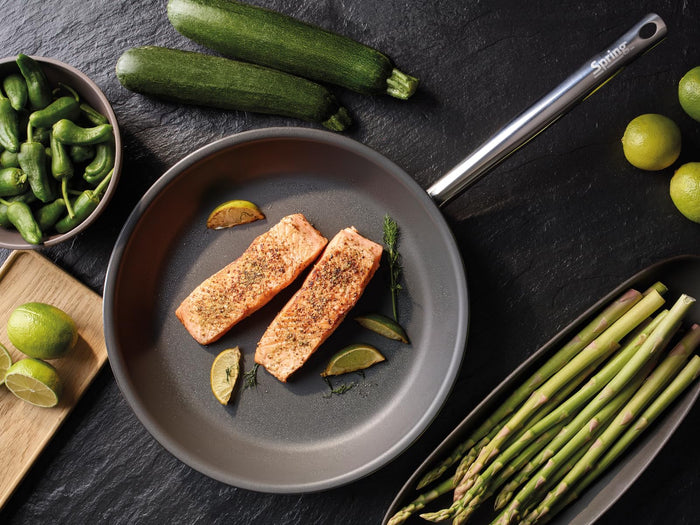 Salmon fillets in a pan with vegetables on a dark surface