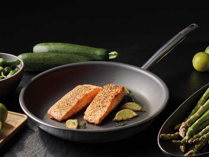 Salmon fillets in a frying pan with vegetables on a dark surface