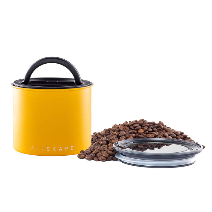 Matte yellow-colored coffee canister with lid, coffee beans, and a clear container on a white background