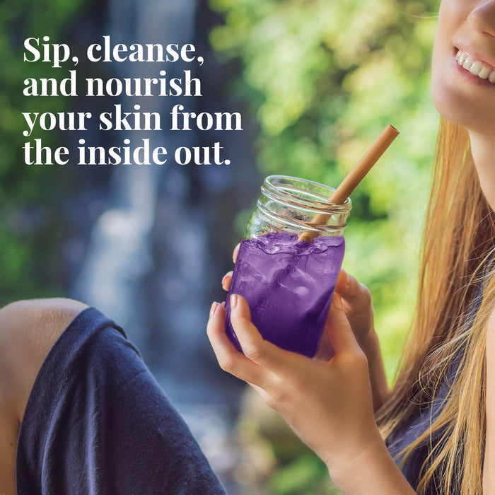 Person holding a purple drink in a mason jar with a straw, outdoors.