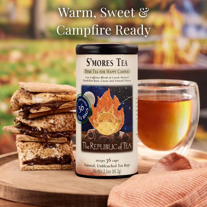 S'mores tea packaging with s'mores and a cup of tea on a wooden surface with a blurred campfire in the background.
