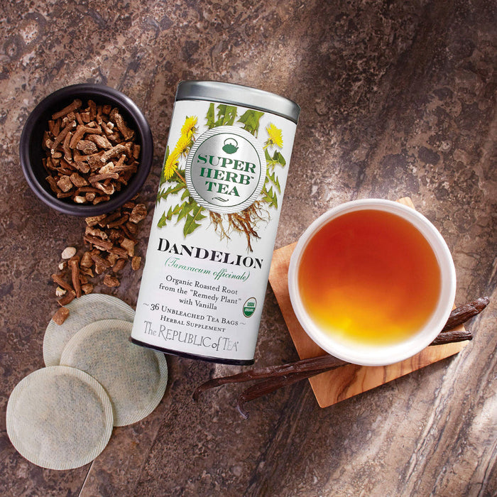 Top view of Super Herb Tea Dandelion tin next to herbs, 3 tea bags, and a mug of tea displayed on a wooden surface