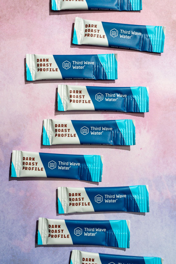 Multiple packages of Third Wave Water with 'Dark Roast Profile' on a pink and purple gradient background.