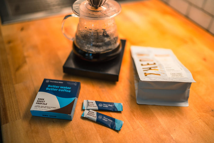 Coffee-making setup with a coffeepot, packets of coffee, and a box on a wooden surface.