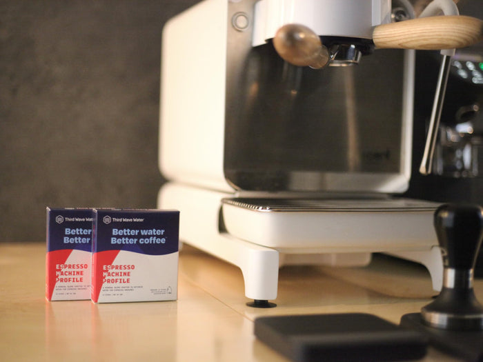 Espresso machine with two boxes of Third Wave Water Espresso Machine Profile on a wooden surface.