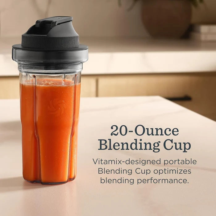 A Vitamix portable blending cup filled with orange juice sits on a light countertop in a kitchen setting. Text on the right reads '20-Ounce Blending Cup' and 'Vitamix-designed portable Blending Cup optimizes blending performance.