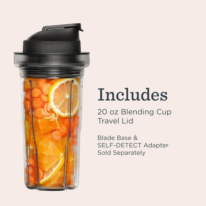 A clear 20 oz blending cup with a black travel lid, filled with orange slices and carrots, shown on a light beige background with text stating it includes the travel lid and blade base.