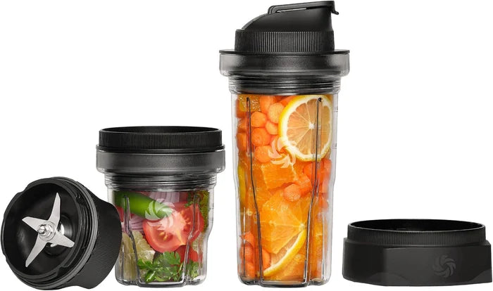 Three clear blending cups with black lids and blades, shown on a white background. The tall cup on the right contains orange slices and carrots, the medium cup in the middle contains mixed greens and red onion, and the short cup on the left shows the exposed silver blades.