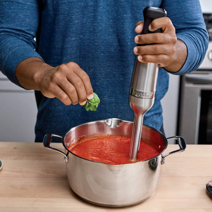 Someone using Vitamix immersion blender in a red paste inside a pot displayed in a kitchen setting