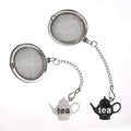 Two round stainless steel tea infuser strainers with hanging silver chains and small teapot-shaped charms, one white and one black, both printed with the word 'tea' on a plain white background.