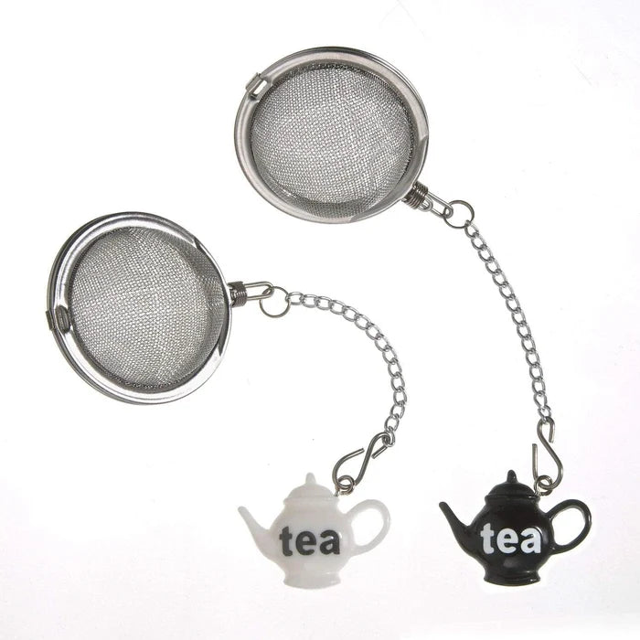 Two round stainless steel tea infuser strainers with hanging silver chains and small teapot-shaped charms, one white and one black, both printed with the word 'tea' on a plain white background.
