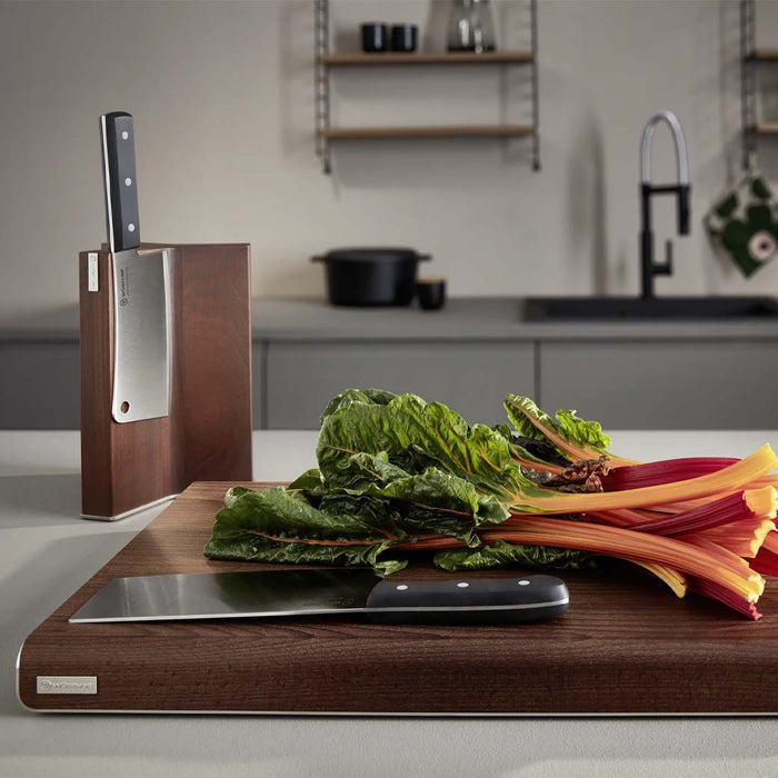2 6 inch Wusthof classic meat cleaver one displayed on a magnetic knife block and other is laid on a wooden cutting next to colorful veggies all placed in a kitchen setting