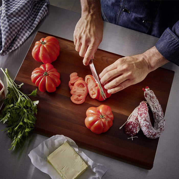 An individual cutting tomatoes with a wusthof knife on a cutting board next to herbs, cream cheese, and sausage