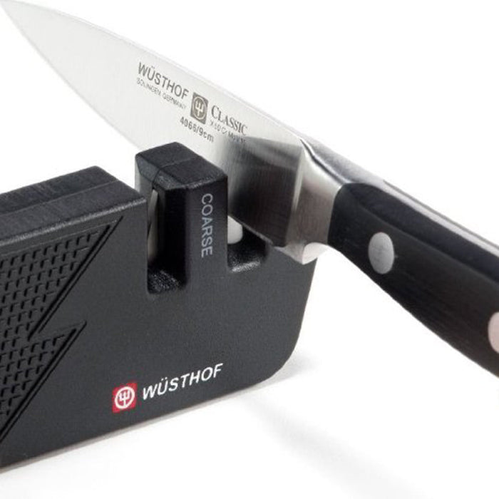 A Wusthof knife being sharpened with a Wusthof black keychain picnic sharpener on a white background
