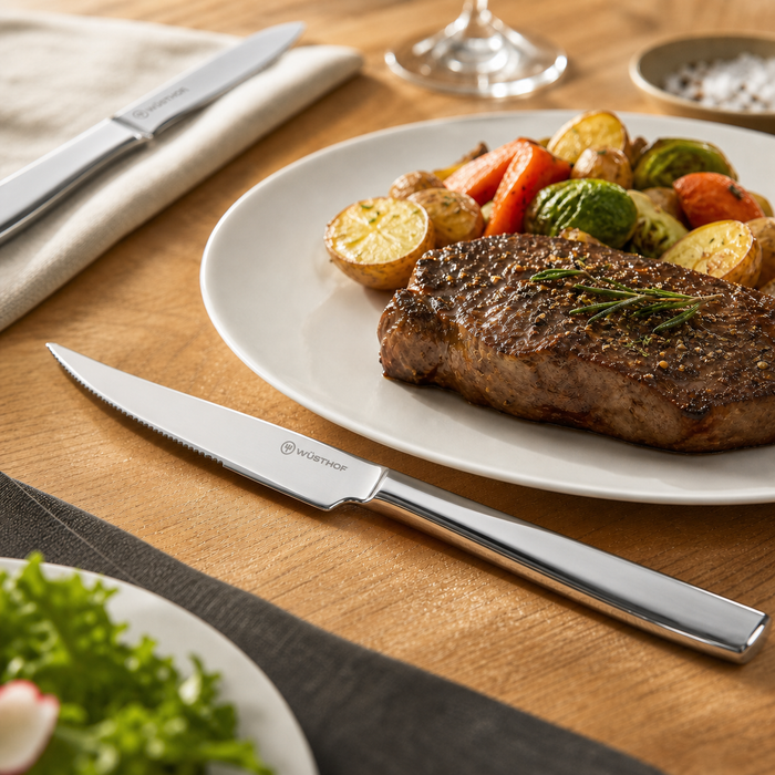 Steak with vegetables on a plate with a Wüsthof knife on a wooden table.