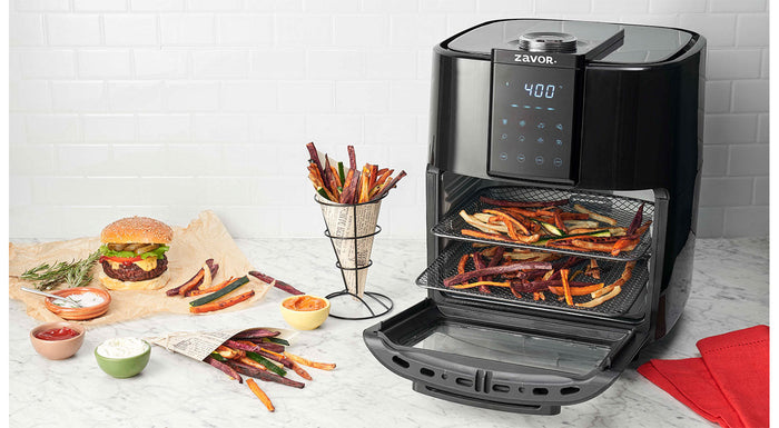 A black Zavor Crunch 12.7 Quart Air Fryer Oven displayed with food items around it, indicating its multifunctional kitchen appliance use.