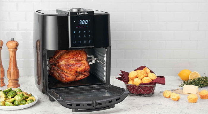 12.7 qt zavor air fryer oven with a chicken being cooked inside with biscuits and brussel sprouts on the side on a marble countertop
