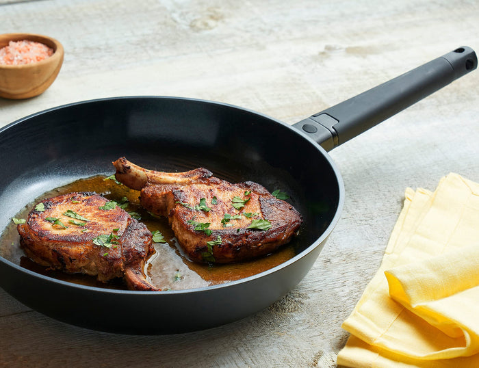 Zavor noir skillet with black handle with food on the skillet and around them with yellow table cloth on a light colored wooden surface