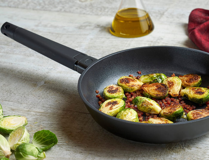 Zavor noir skillet with black handle with food on the skillet and around them on a light colored wooden surface