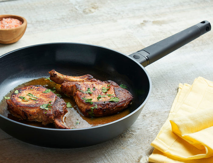Zavor Noir skillet with 2 cooked lamb chops next to a bowl of salt and yellow napkin displayed on a wooden surface