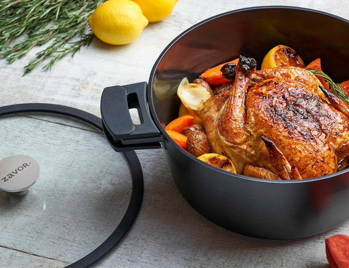 Zavor Noir pan with a cooked turkey next to lemons, herbs, and Zavor lid displayed on a wooden surface