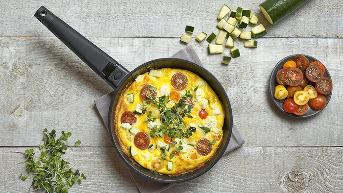 Top view of Zavor skillet with an omelet next to cut vegetables and herbs displayed on a wooden surface