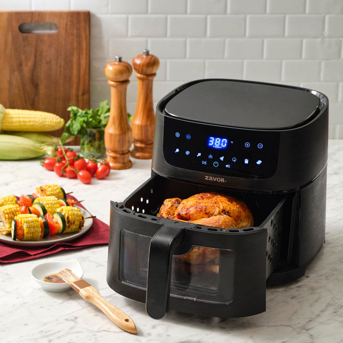Zavor sizzle air fryer oven with a chicken roast on a countertop with fruit and vegetables